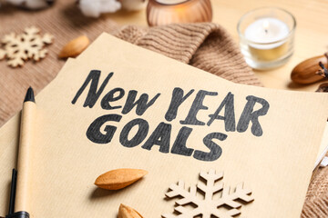 Paper with text NEW YEAR GOALS, sweater and Christmas decor on wooden background, closeup