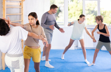 Girls and boys practicing in pair self-defence movements with female trainer supervision