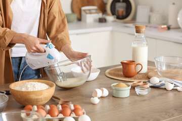Young woman whipping eggs with mixer at table in kitchen