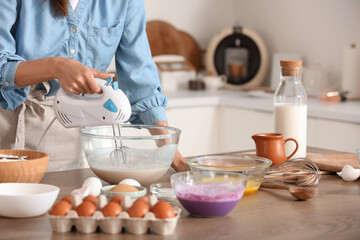 Young woman using mixer at table in kitchen