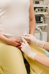 Gynecologist measures pregnant belly with measuring tape to follow the growth of the baby on the appointment. Gynecologist checks size of the woman belly in the clinic.