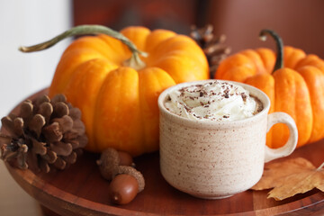 Cup of latte with pumpkins, fir cones and autumn leaf on tray in room, closeup