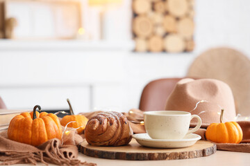 Cup of coffee with croissant and pumpkins on table in room, closeup