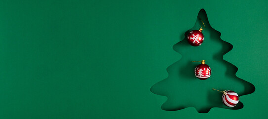 Minimalist Christmas composition with tree cutout and red ornaments on green background. Modern...