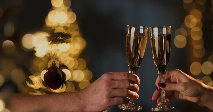 Two champagne flutes clinking against blurred Christmas tree and twinkling lights. Holiday celebration
