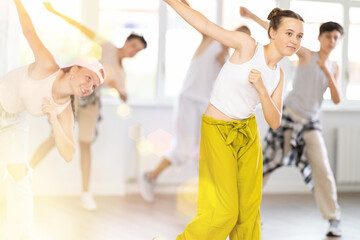 Obraz premium Dynamic teen girl training hip hop slides in dancehall during workout session in group