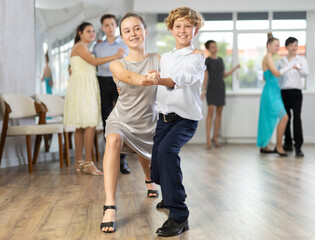 Smiling adolescent girl and boy in formal wear practicing tango in pair, participating in dance...