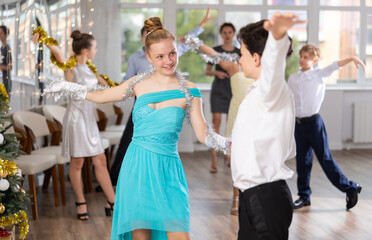 During rehearsal of reporting concert, adolescence boy and girl participants of dance workshop perform quickstep under guidance of female mentor in New Year atmosphere