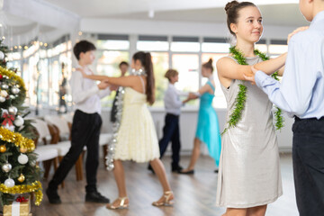 Positive teen boy and girl are dancing classic version of waltz in couple during lesson at studio in New Year atmosphere. Leisure activities and physical activity for positive children.