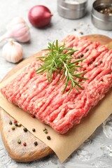 Raw minced meat with rosemary, spices and onion on grey textured table, closeup