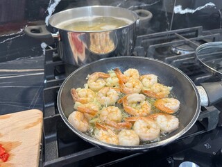 Shrimps and pasta cooking on stove in kitchen, closeup