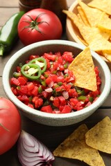 Tasty salsa with nachos and ingredients on wooden table, closeup