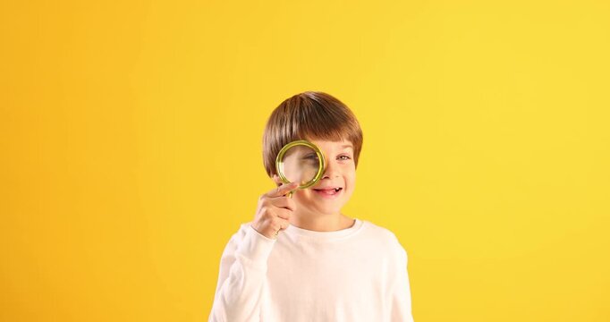 Happy boy looking around through magnifying glass on yellow background