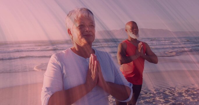 Holding prayer pose yoga practitioners wearing gear standing on beach at sunset with ocean waves