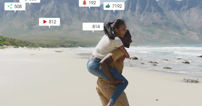 Man carrying partner on back walking along beach near mountains, with floating interaction icons