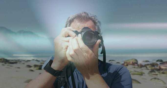 Male photographer capturing coastline at rocky beach, with DSLR camera and fitness tracker