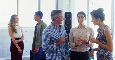 Chatting five coworkers in business-casual attire in lounge with speaker, concrete and city windows
