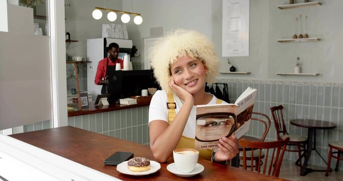 Reading woman wearing yellow dress leaning head on hand at cafe counter, with book and cappuccino - Powered by Adobe