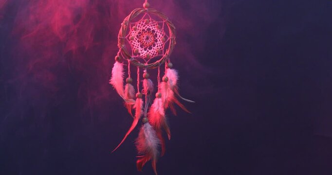 Beautiful dream catcher hanging in color lights on dark background with smoke