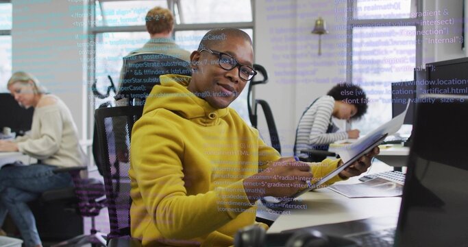 Developer wearing yellow hoodie reviewing printed code documents in modern office, with laptops - Powered by Adobe