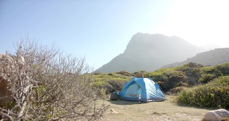 Bright blue tent sitting on grassy clearing at mountain base, with mat, duffel bag, copy space