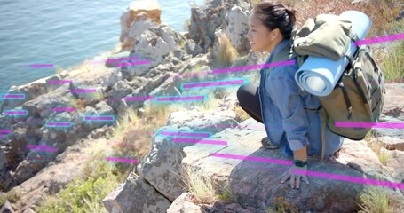 Fototapeta premium Crouching Asian hiker viewing rugged cliffside inlet, carrying backpack with rolled mat, copy space