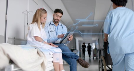 Doctor pointing tablet to patient in hospital corridor with table, IV stand, blanket and wheelchair