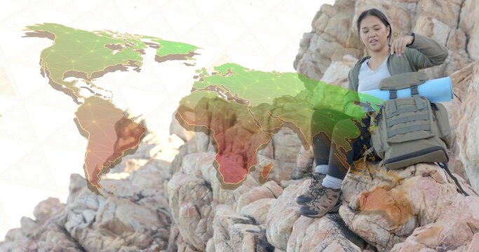 Sitting Asian woman wearing hiking gear on rocky cliff outcrop, with backpack and world map overlay - Powered by Adobe