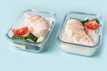 Two glass boxes with rice, chicken fillet and vegetables on blue background, meal planning concept.