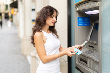 Young woman in summer dress withdraws cash from an ATM on city street