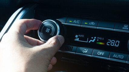 Man hand adjusting the temperature of a car climate control panel. Control panel has a digital display of temperature level and wind speed.