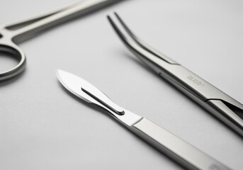 Modern surgical scalpel and forceps arranged diagonally on a sterile white surface, close up