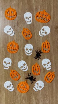 Vertical Halloween concept: glowing skeleton hands placing spiders with white skulls and pumpkins on a black background.