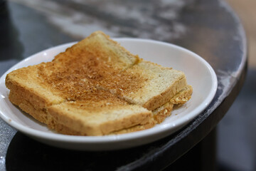 pieces of crispy Kaya Toast, a traditional sweet sandwich filled with coconut jam and butter, served on a white plate in a Malaysian or Singaporean Kopitiam for breakfast.