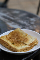 pieces of crispy Kaya Toast, a traditional sweet sandwich filled with coconut jam and butter, served on a white plate in a Malaysian or Singaporean Kopitiam for breakfast.