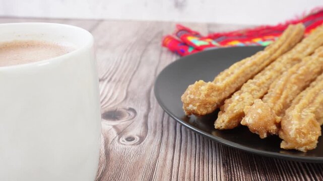 Panning to a table with a cup of hot chocolate and churros on a plate, Mexican food