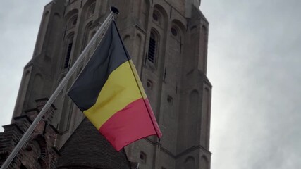 Footage of the Belgium national flag waving against a cloudy sky from a historic church tower. Represents national identity, patriotism, and European heritage.