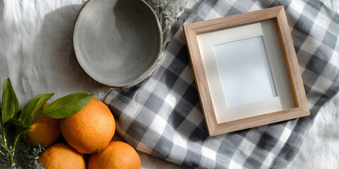 Still life of oranges with wooden frame, a bowl, and checked pattern cloth. The scene is bathed in natural light.