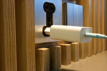 Close-up a cell phone charger with a soft blue data cable plugged into a socket next to the night light switch, Close-up view of plugging a cell phone charger into a wall outlet to charge the phone