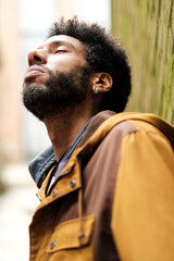 Young man breathing fresh air, leaning against a wall, enjoying a moment of peace