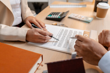 A real estate agent and a client are discussing and pointing at a housing contract document during a property purchase meeting, showing agreement details and financial negotiation about home ownership