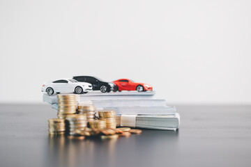 Three car models in red, black and white placed on stacks of money with scattered coins,...