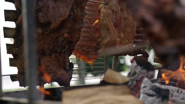 Argentinian meat barbecue cooking over flames in traditional asado with smoke and coals, slow motion detailed cooking