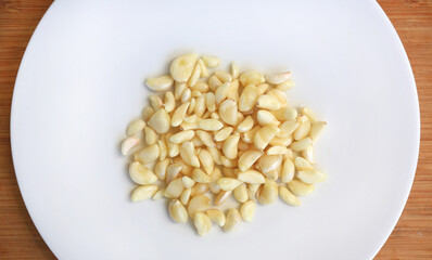 Peeled garlic cloves on white plate against wooden background, preparation process of garlic for cooking. Top view.