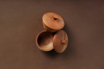 A wooden bowl complete with its cover sits against a rich brown backdrop