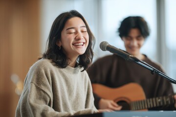 Joyful Asian young adult singing passionately into a microphone, with a blurred guitarist in the background.