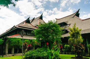 The iconic architecture of the ITB Auditorium in Bandung, a colonial-era heritage building. Its distinctive roof blends beautifully with lush, green climbing plants.