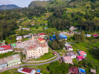 An aerial view of the mountain town of Maubisse in Ainaro, Timor-Leste. A historic old church stands at the center of the village, surrounded by the vast green highland landscape.