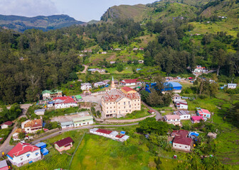 An aerial view of the mountain town of Maubisse in Ainaro, Timor-Leste. A historic old church stands at the center of the village, surrounded by the vast green highland landscape.
