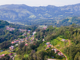 A stunning aerial view of Maubisse village in the highlands of Ainaro, Timor-Leste. Houses are scattered across the ridges and valleys, surrounded by a vast, green mountain landscape
